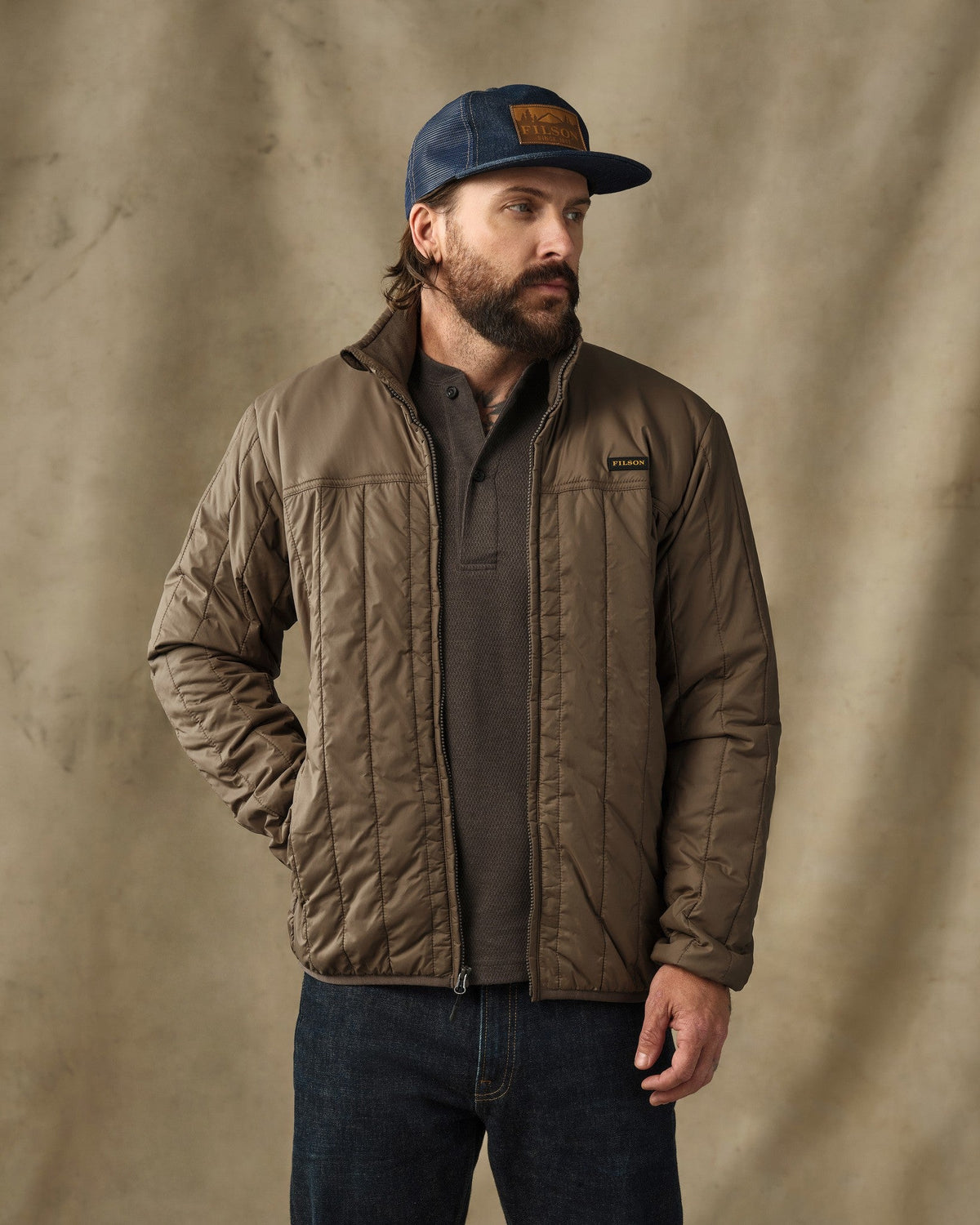 Man wearing olive quilted Filson Ultralight Jacket with navy cap and dark jeans