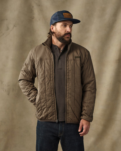 Man wearing olive quilted Filson Ultralight Jacket with navy cap and dark jeans