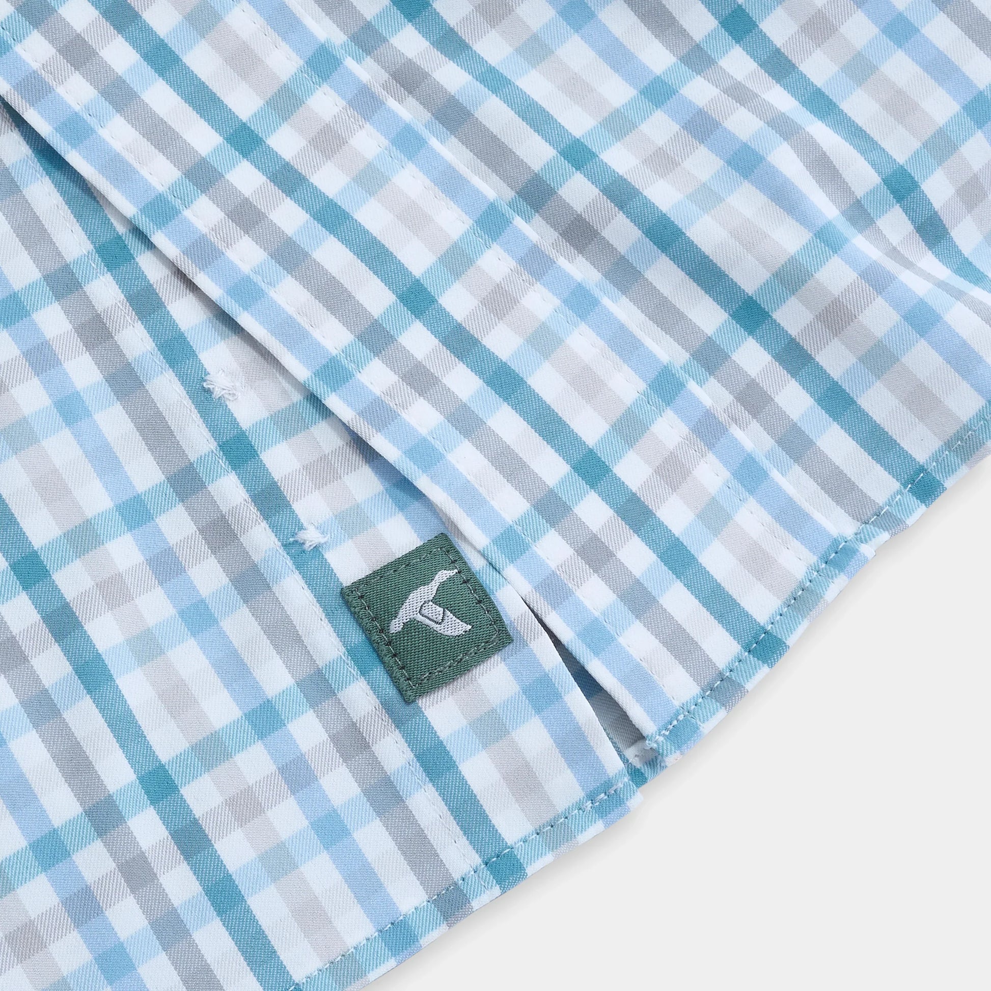 Blue and white plaid button-down shirt hem with small green woven brand label